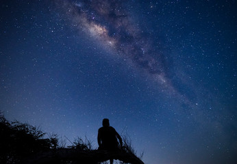 Fototapeta na wymiar Person sitting on a tree branch at night enjoying milky way and sky full of stars dreamy moment at campsite in Sumbawa