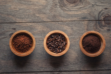 Three types of coffee :instant, grounded and beans in wooden bowls on wooden table, top view with copy space