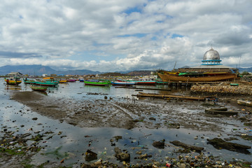 Sape harbour fishing town scene on low tide many traditional wooden boats in dirty water mosque and mountains in Sumbawa