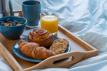 Breakfast served in bed on wooden tray with coffee and croissants close up. Good morning concept