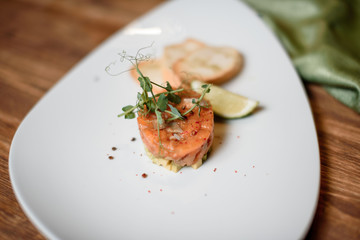 salmon tartar with garlic and lime on white dish wooden table