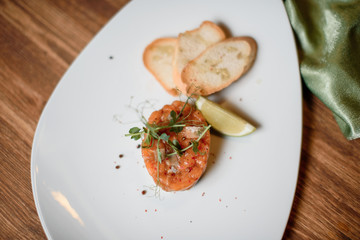 salmon tartar with garlic and lime on white dish wooden table