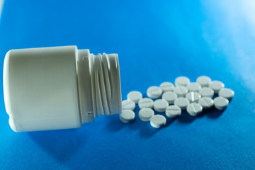 White tablets are dispersed from a bottle on a blue background