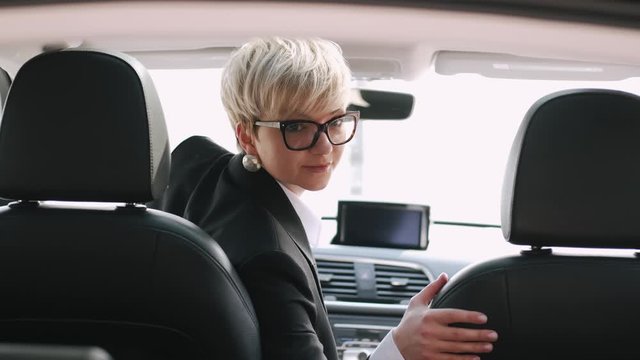 A businesswoman id driving a car. She is about to back up and looking at the front mirror.