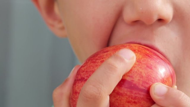 Boy bites and chews red apple, close up macro video