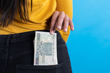 A young woman inserts a bundle of paper banknotes into the back pocket of jeans.