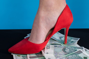 A female foot in a red high heel presses a bundle of money. - obrazy, fototapety, plakaty