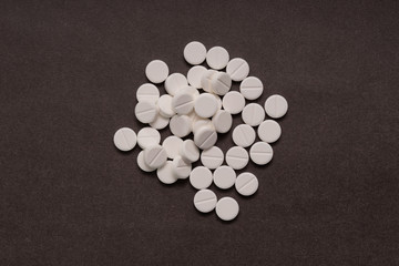 White tablets are scattered from a bottle on a brown background.