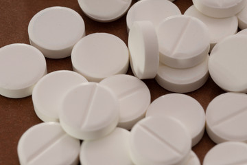 White tablets are scattered from a bottle on a brown background.