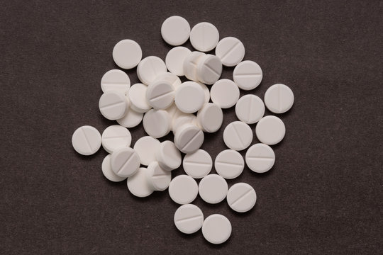 White tablets are scattered from a bottle on a brown background. © zerbob2