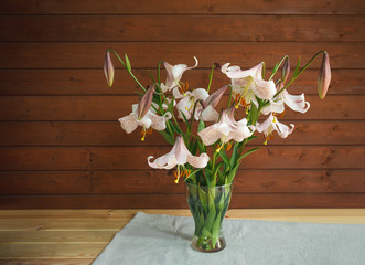Bouquet of beige colored lilies with pink spots in glass  vase. Wooden background.
