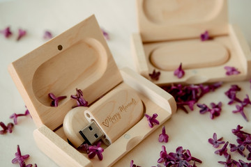 Wooden brown usb flash drives with boxes with the text Happy Moments with lilac petals on a white background, data storage, beautiful feedback to client.
