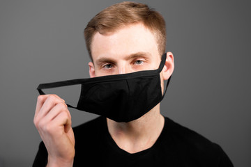 Handsome man in black t-shirt wear black medical mask, gray background. Coronavirus covid-19 quarantine period concept.