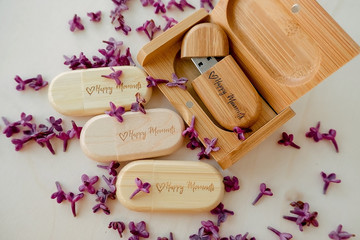 Fototapeta na wymiar Wooden brown usb flash drives with boxes with the text Happy Moments with lilac petals on a white background, data storage, beautiful feedback to client. set for the photographer, presentable set 