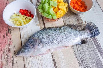 Cooking concept. Barramundi or Asian Sea Bass or Siakap fish close up together on wooden table with other ingredients.