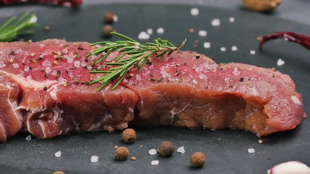 Beef sirloin raw steaks with spices on a dark table.