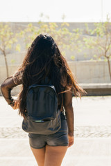 Girl with long hair with a backpack and summer clothes walking down the street