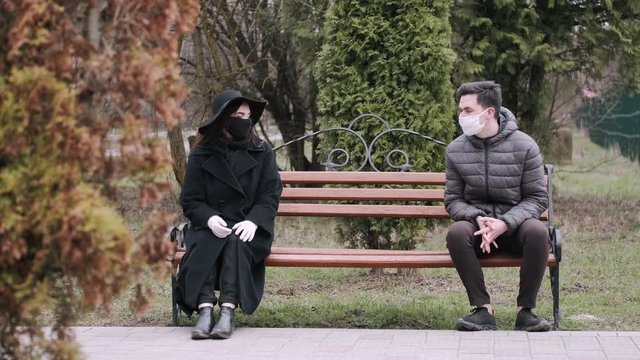 The lady and a man have met on quarantine. They are keeping social distance and sitting at the ends of a bench while talking.