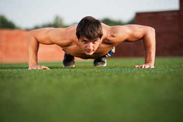 Fototapeta premium Outdoor sport, fitness training. Handsome Young Men Doing Pushups Outdoors in the Sport Field on a Sunny day