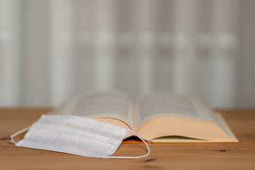 A thick book with open hardcover on the shelf , one surgical mask on the shelf 