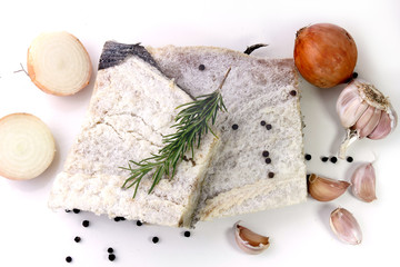 dry salted raw cod isolated over white background, accompanied by pepper, onion, garlic, parsley, spices