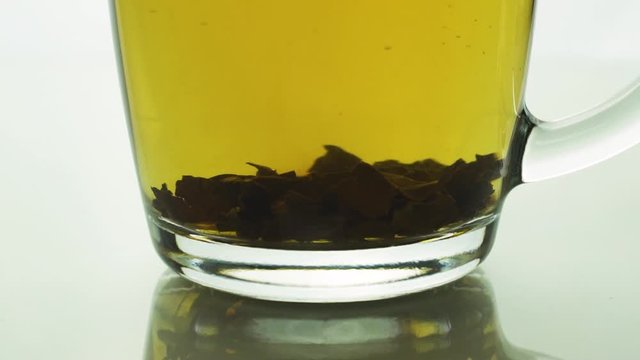 black tea particles spinning at bottom transparent glass mug creating a whirl, brewing tea slow motion close up .