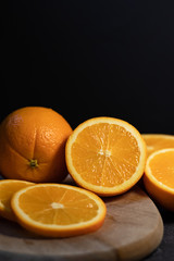 Sliced orange citrus fruit on a wooden board on a dark background.