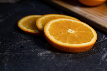Sliced orange citrus fruit on a wooden board on a dark background.
