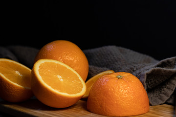 Sliced orange citrus fruit on a wooden board with a gray towel on a dark background.