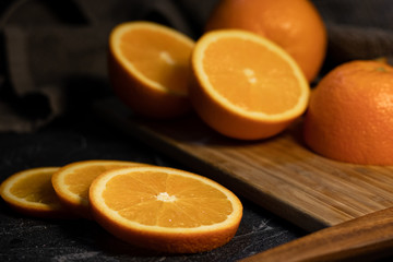 Sliced orange citrus fruit on a wooden board on a dark background.