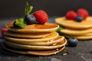 Close-up of a stack of pancakes with berries (blueberries, raspberries), honey and mint on a dark background.