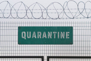 Quarantine sign on barbed wire fence, a digital composite. Tough lockdown measures restrict rights of people as well as ruin economics in many countries during the coronavirus (COVID-19) epidemic.