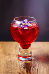 Tasty red cocktail with pieces of ice, strawberry syrup in a transparent glass on a wooden table. Copy space