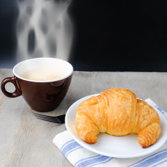Croissant on white plate and coffee on wooden rustic background. the view from the top