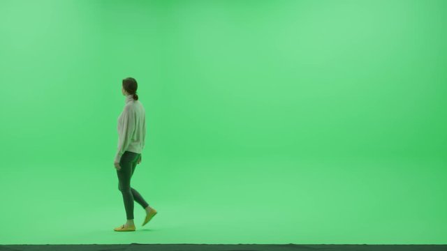 Green Screen Chroma Key Studio: Beautiful Young Woman Wearing Stylish Casual Clothes Walks Across Room Right to Left. Side View Camera Shot