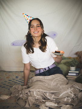 Portrait of happy Caucasian teenage girl on her birthday wearing birthday hat and holding brownie with a single candle.  Sweet sixteen but alone.