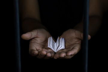 Diminuto libro en un par de manos frente a una ventana con fondo negro 