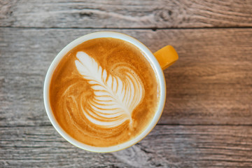Coffee art, in a yellow cup, on the wooden floor