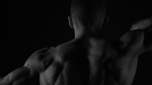 Strong bodybuilder posing and training in contrast light showing his body and every muscle on it under water drops and slow rain