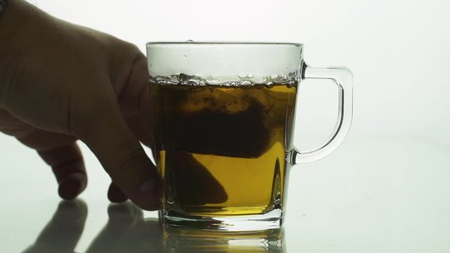 man&rsquo;s hand lifting and dropping black tea bag into glass transparent mug to brew tea isolated on white background slow motion close up.