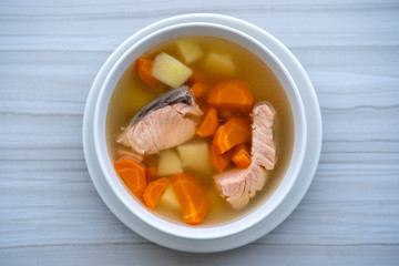 Fresh salmon fish soup with carrots, potatoes and onions in a white plate, close up. Tasty dinner consists of a fish soup with salmon