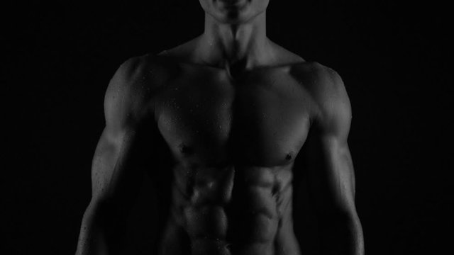 Strong bodybuilder posing and training in contrast light showing his body and every muscle on it under water drops and slow rain