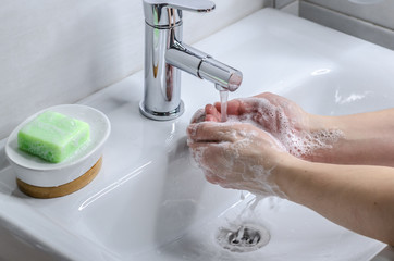 Hand washing with soap. Preventive measures against infection. A young guy washes his hands with soap in the bathroom. Body hygiene. The fight against COVID-19.