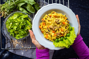 Yellow millet grain porridge with vegetables, herbs, spices and mushrooms. Vegan healthy food. Hands