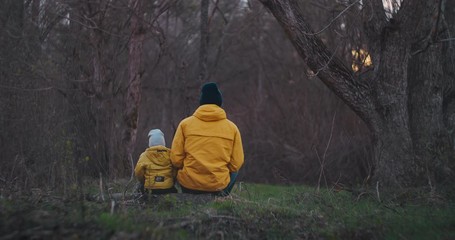 Happy father embracing son while sitting on log at park. Happy father embracing son while sitting on log at wood back to the camera. Slow motion precious moments the closeness of father and young son