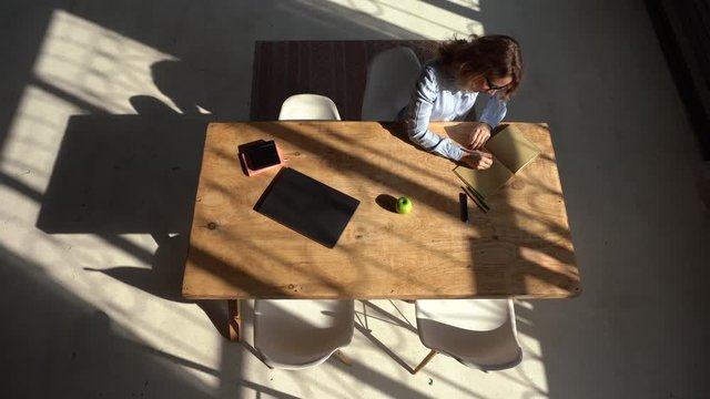Woman draws in a notebook during a break. Working from home. Bright sun with long shadows