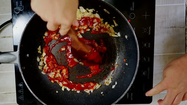 fried garlic , onion and hot chili sauce with wooden turner in induction pan on electric stove, red light indicator power on and fry menu button, high temperature