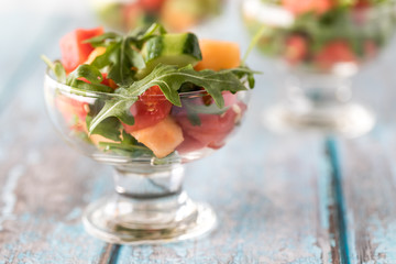 A macro close up view of a glass dish with watermelon and arugula salad ready for eating.