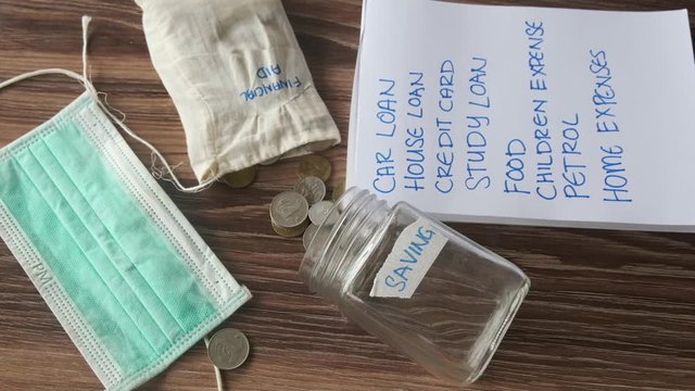 A footage of financial aid bag drop on monthly commitment list with saving container and face mask insight. Financial aid or economic stimulus helps people to survive monthly.