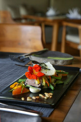 Beautifully arranged tuna sandwich on the black plate, decorated with edible flowers. Exquisite dish, creative restaurant meal concept, haute couture food.